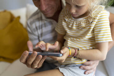 Vater und Tochter benutzen zu Hause gemeinsam ein Mobiltelefon - SVKF01681