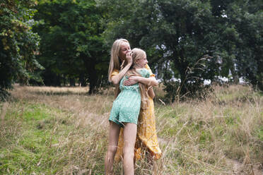 Glückliches Mädchen, das seine Mutter umarmt und auf trockenem Gras im Park steht - AMWF01847