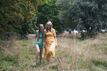 Mother and daughter walking on dry grass in park - AMWF01850