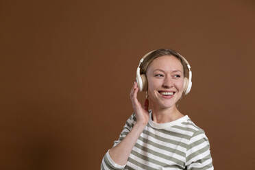 Lächelnde Frau hört Musik über Kopfhörer im Studio - MIKF00412