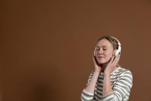 Frau mit geschlossenen Augen hört Musik über Kopfhörer im Studio - MIKF00413