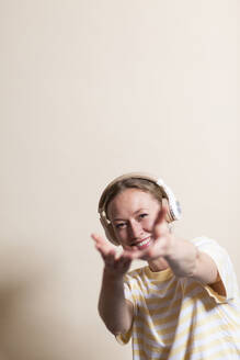 Lächelnde Frau gestikuliert und hört Musik über Kopfhörer im Studio - MIKF00423