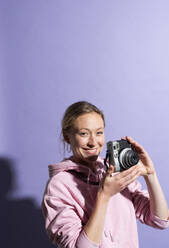 Lächelnde Frau hält Kamera über lila Hintergrund - MIKF00432