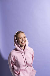 Happy woman smiling with hands behind back over purple background in studio - MIKF00441