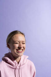 Frau lächelnd mit geschlossenen Augen gegen lila Hintergrund im Studio - MIKF00443