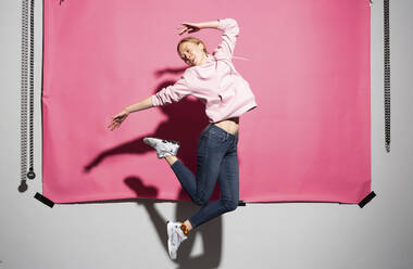 Playful woman jumping against pink background - MIKF00455