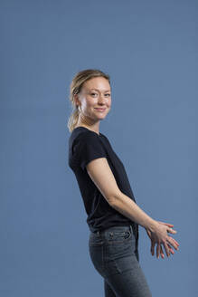 Lächelnde Frau in Jeans, stehend vor blauem Hintergrund - MIKF00463