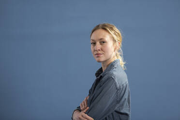 Blond woman with arms crossed against blue background - MIKF00486