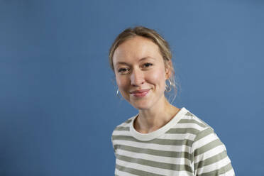 Blond woman wearing striped t-shirt against blue background - MIKF00489