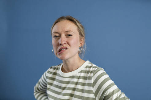 Frau beißt auf Lippe vor blauem Hintergrund - MIKF00500