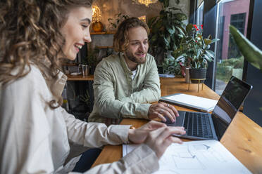 Businessman explaining colleague over laptop sitting at cafe - VPIF08721