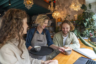 Lächelnde Kellnerin serviert Kaffee an Geschäftskollegen in einem Café - VPIF08727