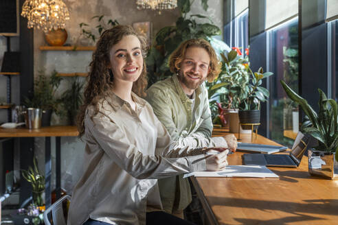 Lächelnde junge Geschäftskollegen sitzen am Tisch in einem Café - VPIF08735
