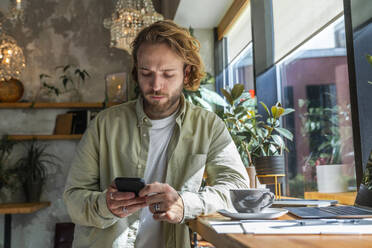 Businessman using smart phone leaning on desk at cafe - VPIF08738