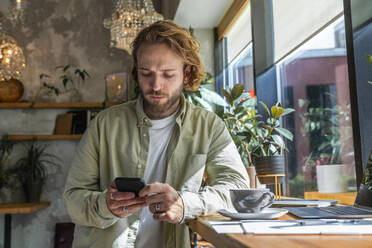 Geschäftsmann, der ein Smartphone benutzt und sich in einem Café auf den Schreibtisch lehnt - VPIF08738