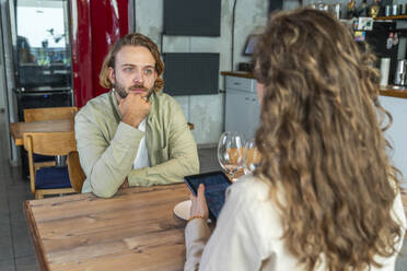 Mann mit Hand am Kinn sieht Freundin im Café sitzend an - VPIF08751