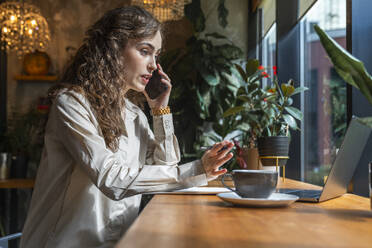Konzentrierte Geschäftsfrau, die in einem Café mit ihrem Smartphone telefoniert - VPIF08762
