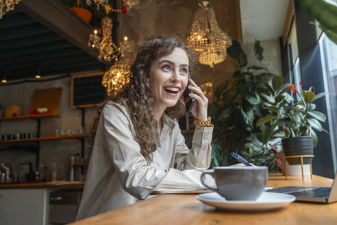 Glückliche Geschäftsfrau, die in einem Café sitzt und mit ihrem Handy spricht - VPIF08764