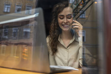 Glückliche junge Geschäftsfrau im Gespräch mit Smartphone durch Glas gesehen - VPIF08768