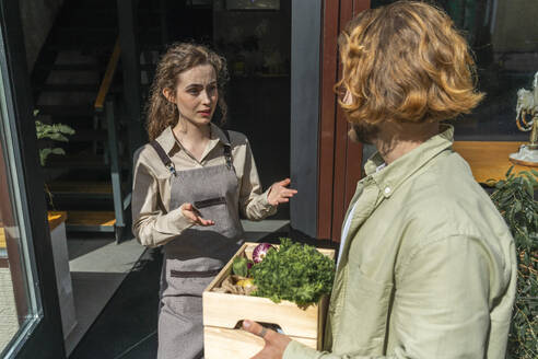 Owner talking with customer holding crate of vegetables outside store - VPIF08774