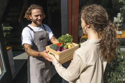 Young owner giving vegetable crate to customer - VPIF08781