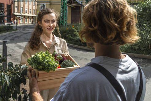 Smiling customer receiving vegetable crate from owner - VPIF08783