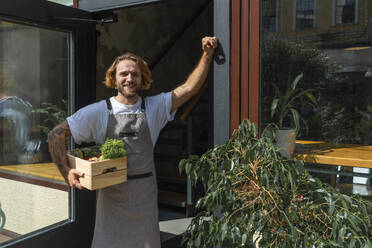 Smiling owner holding vegetable crate standing at store entrance - VPIF08786