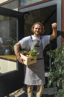 Young owner holding vegetable crate near store entrance - VPIF08787