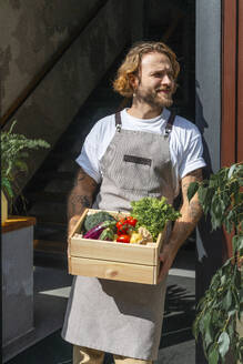 Owner holding fresh vegetables in crate at store doorway - VPIF08788
