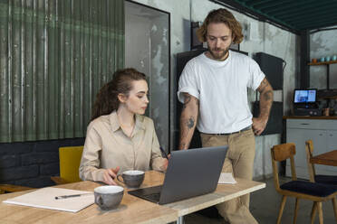 Businesswoman standing by colleague sitting with laptop on table at cafe - VPIF08799