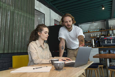 Businessman explaining colleague over laptop at cafe - VPIF08800