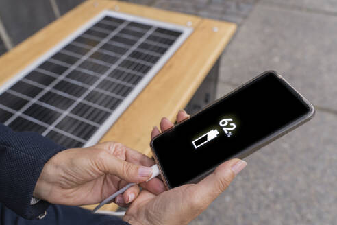 Hände einer Geschäftsfrau, die ihr Smartphone mit Solarenergie auf einer Bank auflädt - OSF02185