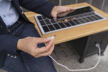 Businesswoman plugging USB cable in smart phone at solar charging point - OSF02186