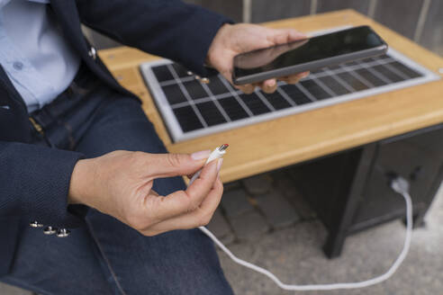 Geschäftsfrau steckt USB-Kabel in Smartphone an Solarladestation - OSF02186