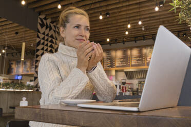Nachdenkliche Geschäftsfrau mit Laptop bei einer Tasse Kaffee im Café - OSF02201