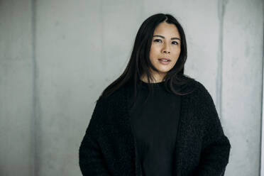 Confident businesswoman in front of wall at workplace - JOSEF21341