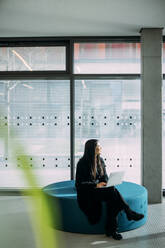 Businesswoman sitting on seat with laptop day dreaming in office - JOSEF21350