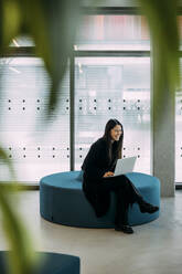 Glückliche Geschäftsfrau auf dem Stuhl sitzend mit Laptop im Büro - JOSEF21351