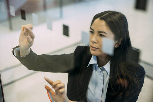 Businesswoman touching glass wall at workplace - JOSEF21425