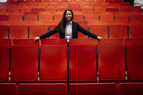Lächelnde Geschäftsfrau inmitten von roten Sitzen im Auditorium - JOSEF21453