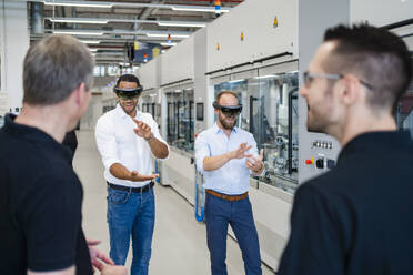 Kollegen beobachten zwei Techniker mit Augmented-Reality-Brillen in einer Fabrik - DIGF20575