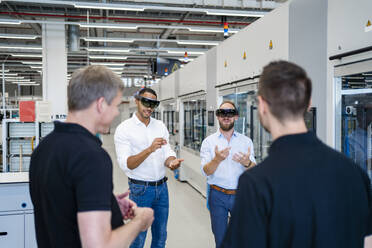 Kollegen beobachten zwei Techniker mit Augmented-Reality-Brillen in einer Fabrik - DIGF20576