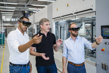 Two technicians wearing augmented reality glasses in a factory and interacting with colleague - DIGF20577
