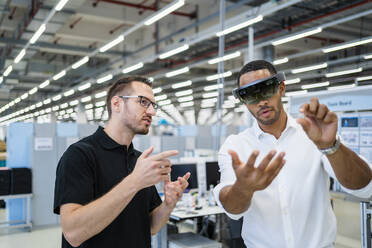 Technician wearing augmented reality glasses in a factory interacting with colleague - DIGF20579