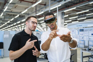 Technician wearing augmented reality glasses in a factory interacting with colleague - DIGF20580