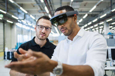 Technician wearing augmented reality glasses in a factory interacting with colleague - DIGF20582