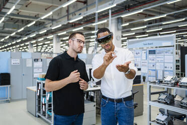 Technician wearing augmented reality glasses in a factory interacting with colleague - DIGF20583