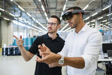 Technician wearing augmented reality glasses in a factory interacting with colleague - DIGF20584