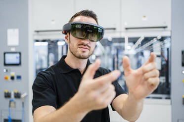 Technician wearing augmented reality glasses and gesturing in a factory - DIGF20585