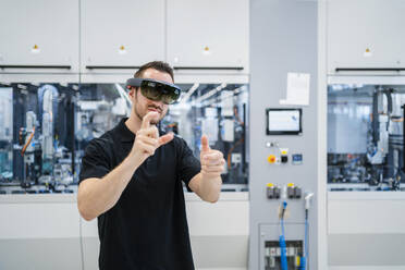Technician wearing augmented reality glasses and gesturing in a factory - DIGF20587